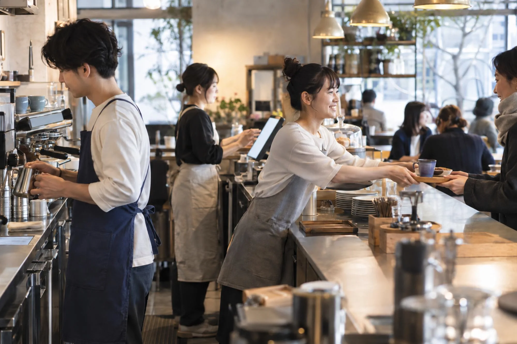 昼どきのカフェで、足りた人数の3人のスタッフが落ち着いて分担して働く（イメージ・見本）